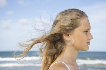 Caucasian pre-teen girl on beach with hair blowing in wind.