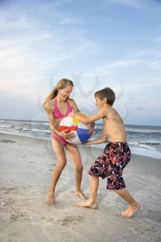 Caucasian pre-teen boy and girl pulling on beachball.