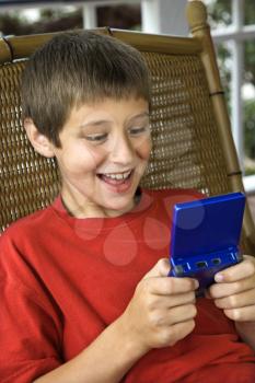 Royalty Free Photo of a Preteen Boy Playing a Hand Held Video Game and Smiling