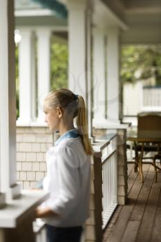 Royalty Free Photo of a Side View of a Preteen Girl Standing on a Porch