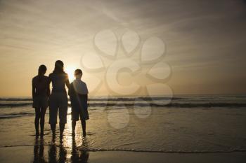 Royalty Free Photo of a Caucasian Mother and Teenage Kids Standing Silhouetted on the Beach at Sunset