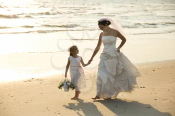 Royalty Free Photo of a Bride and Flower Girl Holding Hands Walking Barefoot on a Beach