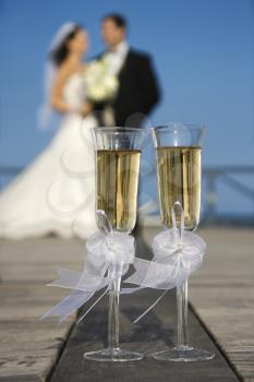 Royalty Free Photo of a Pair of Flute Glasses of Champagne With a Bride and Groom in the Background