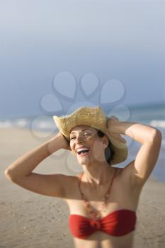 Royalty Free Photo of a Woman Laughing on a Beach in Holding a Hat on Her Head