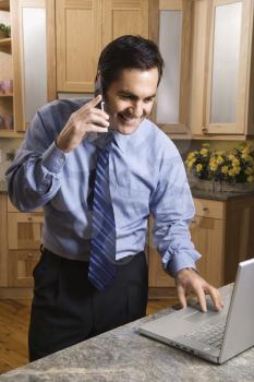 Royalty Free Photo of a male talking on cellphone and looking at laptop computer in kitchen