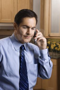 Royalty Free Photo of a Male With a Serious Expression Holding a Cellphone While Standing in the Kitchen