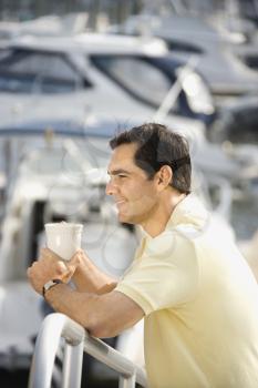 Portrait of Caucasian mid-adult male holding coffee cup at harbor.