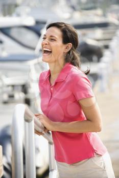 Royalty Free Photo of a Woman Holding a Railing and Laughing at a Harbor