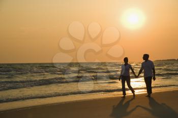Royalty Free Photo of a Couple Holding Hands and Walking Down the Beach at Sunset