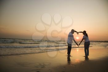 Royalty Free Photo of a Couple Making a Heart Shape With Their Arms on a Beach at Sunset