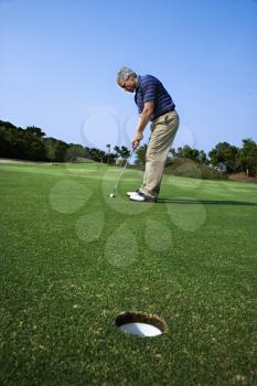 Royalty Free Photo of a Man Putting a Golf Ball With a Hole in The Foreground