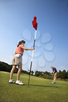 Royalty Free Photo of a Man Putting a Golf Ball While a Woman Holds a Flag