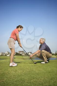 Royalty Free Photo of a Woman Holding a Golf Club While a Man Kneels Holding a Club Teaching