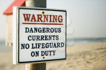 Warning sign on post at the beach with ocean in background.