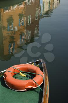 Partial view of bow of boat with reflection of buildings in water in background.