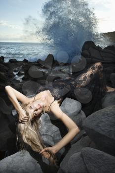 Portrait of Caucasian young adult woman lying on back on rocky coast with hair hanging down making eye contact.