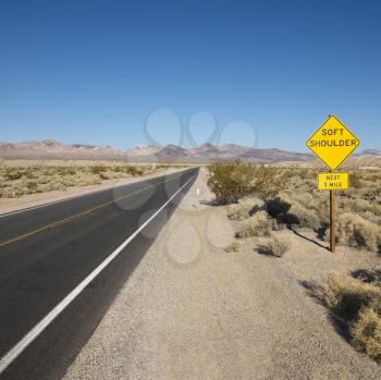 Royalty Free Photo of a Road in a Desert With a Sign for Soft Shoulder and Mountains in the Distance