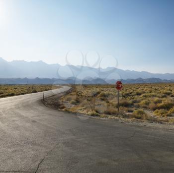 Royalty Free Photo of a Road With a Stop Sign in a Barren Landscape With Mountains in the Distance