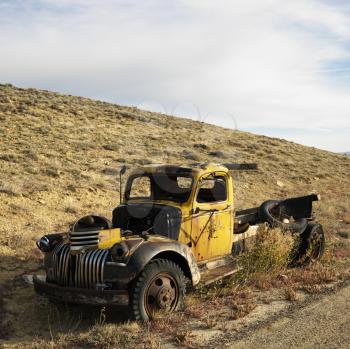 Royalty Free Photo of an Old Yellow Dilapidated Pickup Truck Sitting Abandoned on a Hill.