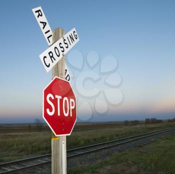 Royalty Free Photo of a Railroad Crossing and Stop Signs Beside Railroad Tracks in a Rural Setting