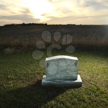 Royalty Free Photo of a Headstone Marking a Grave in a Rural Countryside at Sunset