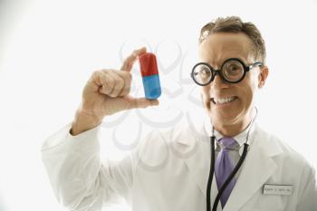 Mid-adult Caucasian male doctor wearing eyeglasses holding an oversized medical pill.