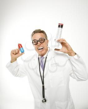Mid-adult Caucasian male doctor wearing eyeglasses holding an oversized medical pill and syringe.