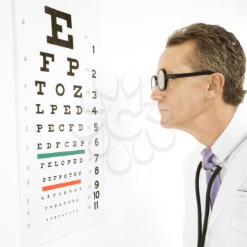 Royalty Free Photo of a male doctor wearing eyeglasses looking at an eye chart