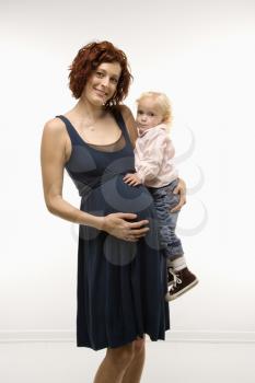 Royalty Free Photo of a Portrait of an Attractive Pregnant Woman Standing, Holding a Female Toddler on her Hip and Other Hand on Her Belly