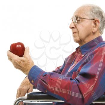 Royalty Free Photo of an Elderly Man Sitting in a Wheelchair Looking at a Red Apple in His Hand