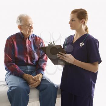 Royalty Free Photo of a Woman in Scrubs Taking Notes from an Elderly Man