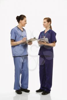Royalty Free Photo of Female Doctors in Medical Scrubs Standing, Talking, Holding Medical Charts 