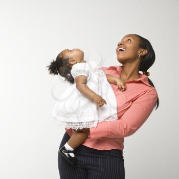 African American woman holding infant girl standing against white background.