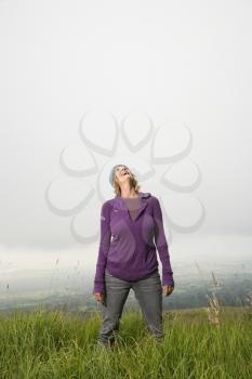 Royalty Free Photo of a Woman Standing Alone in a Field With Her Head Back Laughing
