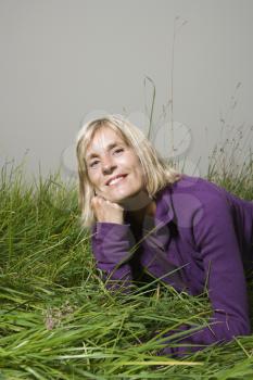 Royalty Free Photo of a Middle-aged Woman Lying in the Grass Resting Her Head on Her Hand Smiling