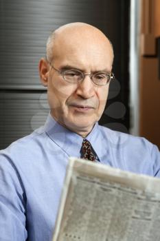 Royalty Free Photo of a Middle-Aged Businessman Sitting in an Office Reading a Newspaper