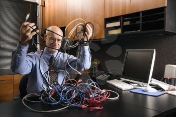 Royalty Free Photo of a Businessman Sitting at a Desk With a Tangle of Computer Cables