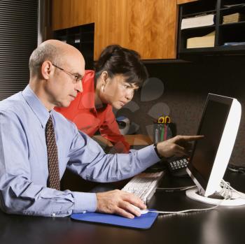 Businessman and businesswoman in office looking and pointing at computer monitor.