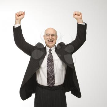 Smiling Caucasian middle-aged businessman jumping with arms raised.