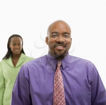 African-American businessman  looking at viewer and smiling with businesswoman in background.