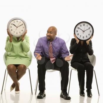Royalty Free Photo of Businesswomen Sitting Holding Clocks Over Their Faces While Businessman Watch