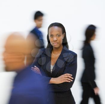 African-American businesswoman standing with arms crossed while others walk by.