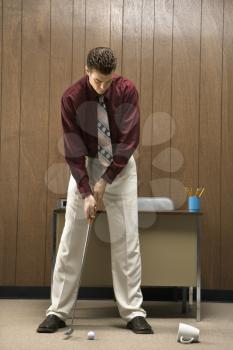Caucasion mid-adult retro businessman putting golf ball into coffee cup in his office.