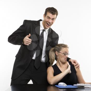 Royalty Free Photo of a Man Sexually Harassing a Woman Sitting at a Computer and Giving a Thumbs Up