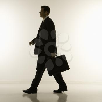 Silhouette of mid-adult Caucasian businessman walking and carrying briefcase.