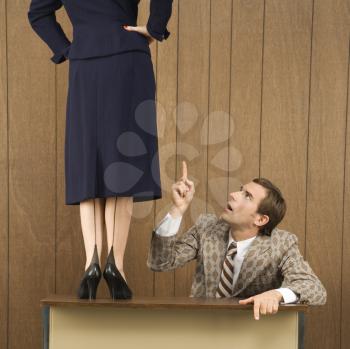 Royalty Free Photo of a Man Pointing Up to a Woman Standing on the Desk