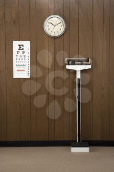 Retro doctor's office with wood paneling, clock, eye chart and scale.