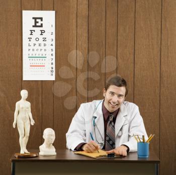 Royalty Free Photo of a Doctor Sitting at a Desk Writing and Smiling