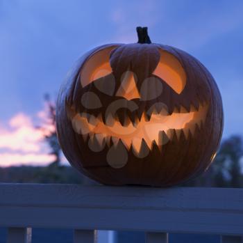 Royalty Free Photo of a Carved Halloween Pumpkin Perched on a Porch Railing