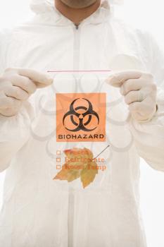 Royalty Free Photo of a Man in a Bio-hazard Suit Holding a Plastic Bio-hazard Bag Containing an Orange Maple Leaf